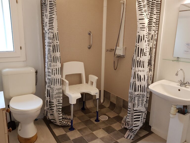 Salle de bain du chalet pour personne à mobilité réduite, avec chaise spéciale et toilettes rehaussées