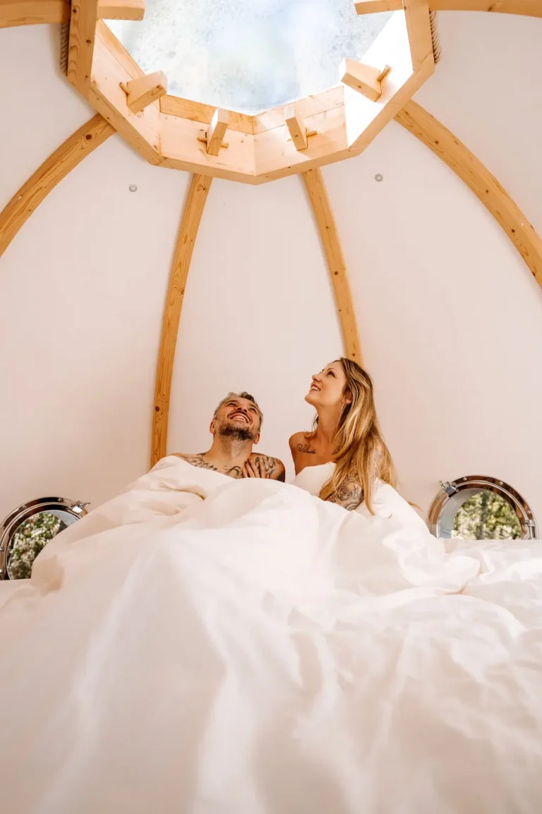 Couple dans le lit du Lov'nid, sous la verrière ouverte sur les arbres