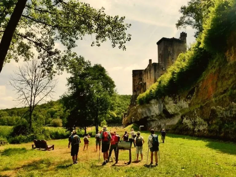 Groupe de randonneurs sous un château perché sur la falaise, vallée de la Dordogne
